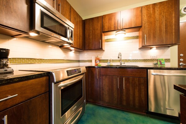 A kitchen with wooden cabinets, stainless steel appliances, and a green tiled backsplash. - Condo in the heart of downtown Austin.- 8th street- (Austin)