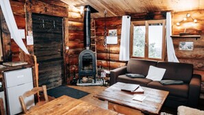 A cozy cabin interior with a wooden interior, a fireplace, a sofa, a dining table, and a refrigerator. - Log cabin Les Convers (Collonges-sous-Salève)
