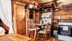A rustic wooden interior with a wooden table and chairs, a stove, and a shelf with kitchen items. - Log cabin Les Convers (Collonges-sous-Salève)