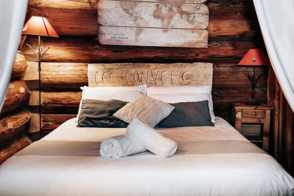 A cozy log cabin bedroom with a bed, pillows, and a world map on the wall.