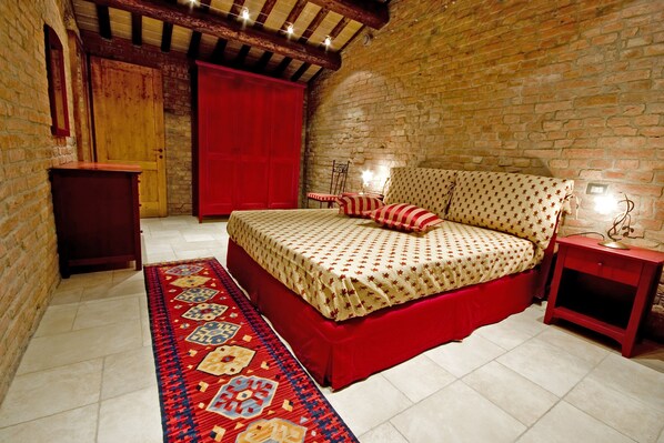 Un dormitorio con una cama grande, un armario rojo, una mesita pequeña y un tapete estampado.