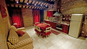Una cocina acogedora con zona de comedor, que presenta una pared de piedra, vigas de madera y una decoración en tonos rojo y blanco.