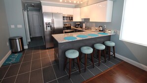 Una cocina moderna con una isla central, taburetes de bar, electrodomésticos de acero inoxidable y vistas al exterior.