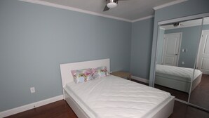 Un dormitorio con una cama, una mesita de noche, un espejo y un ventilador de techo.