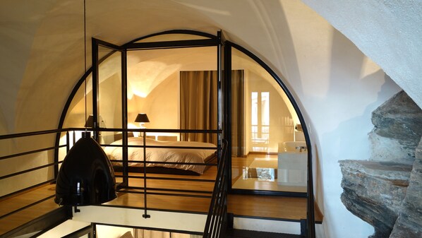 A room with a bed, a nightstand, a lamp, and a view of another room through a glass door. - Loft of 100 m2 in the village of Erbalunga, waterfront (Brando)