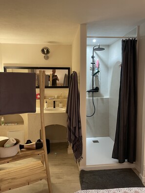 Ein Badezimmer mit Dusche, Waschbecken und Spiegel. Ein Handtuchhalter und ein Ablagefach mit Pflegeprodukten sind vorhanden.