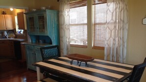 Una mesa de comedor con un banco, un aparador azul y una ventana con cortinas.