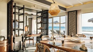 A spacious dining area with a view of the ocean, featuring a wooden table, wicker chairs, and a hanging light fixture.
