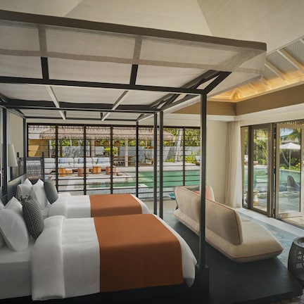 A hotel room with a large bed, a sofa, a small table, and a view of a pool and outdoor area.