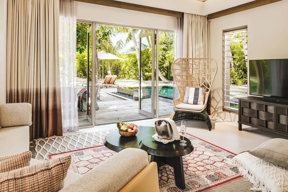A spacious living room with a large TV, comfortable seating, a dining area, and a view of an outdoor pool area.
