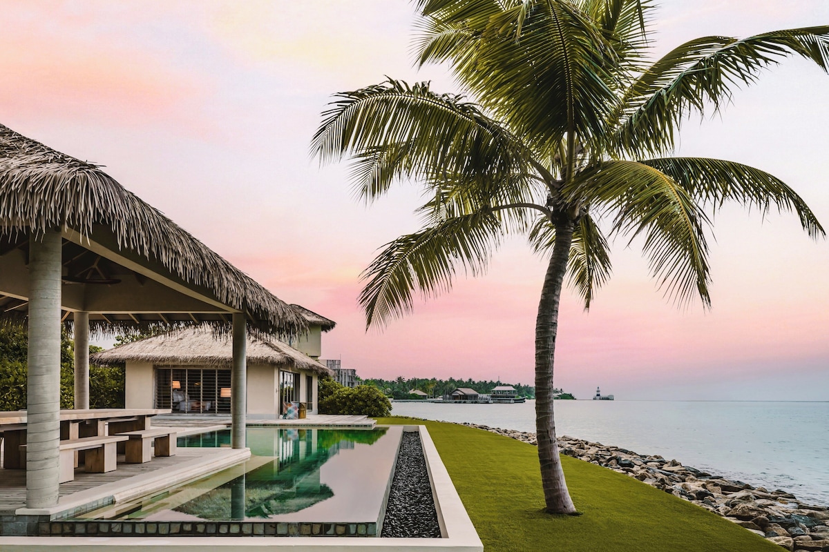 A resort with a pool, palm trees, and a view of the sea.