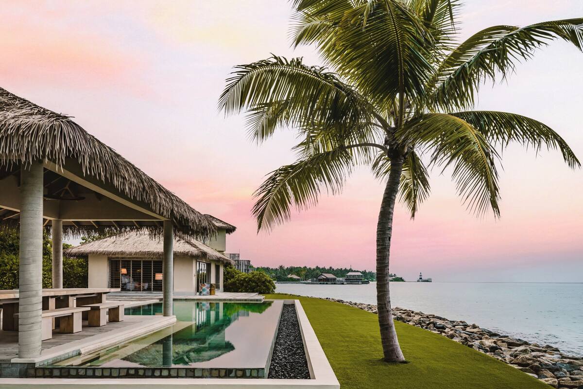 A resort with a pool, palm trees, and a view of the sea.