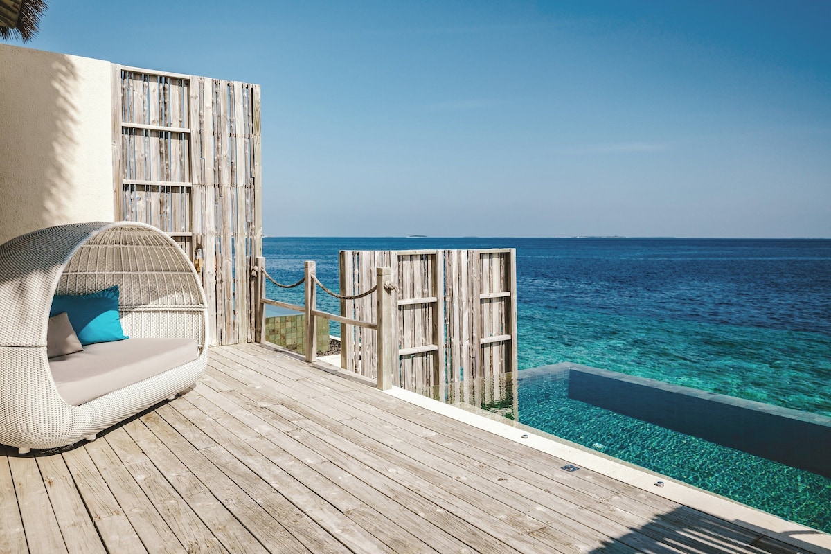 A wooden deck with a wicker chair and a view of the ocean.