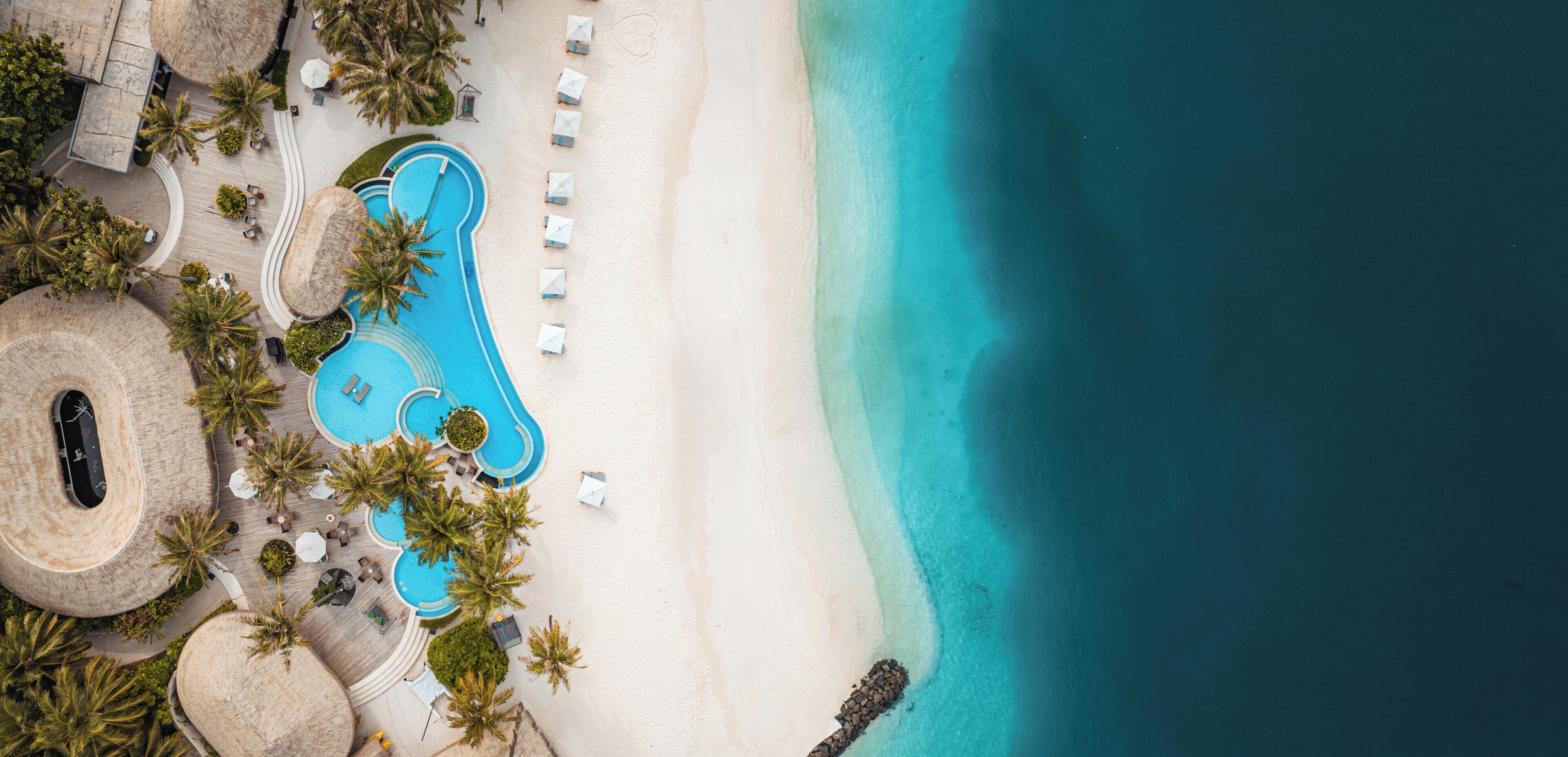 Vista aérea de un resort con piscina, playa y palmeras.