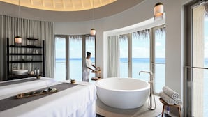 A modern hotel room with a large bathtub, a bed, a vanity with toiletries, and a view of the sea. - InterContinental Maldives Maamunagau Resort by IHG (Maamunagau Island)
