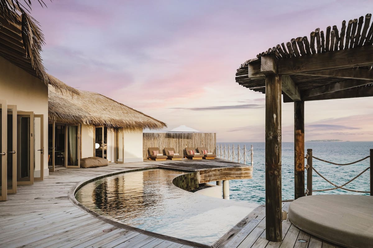 An infinity pool with a wooden deck, a thatched-roof structure, and a view of the sea.
