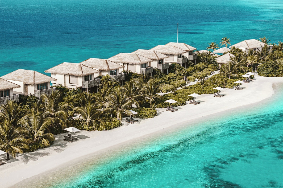 An aerial view of a beach resort with overwater bungalows, white sandy beaches, and clear turquoise waters.