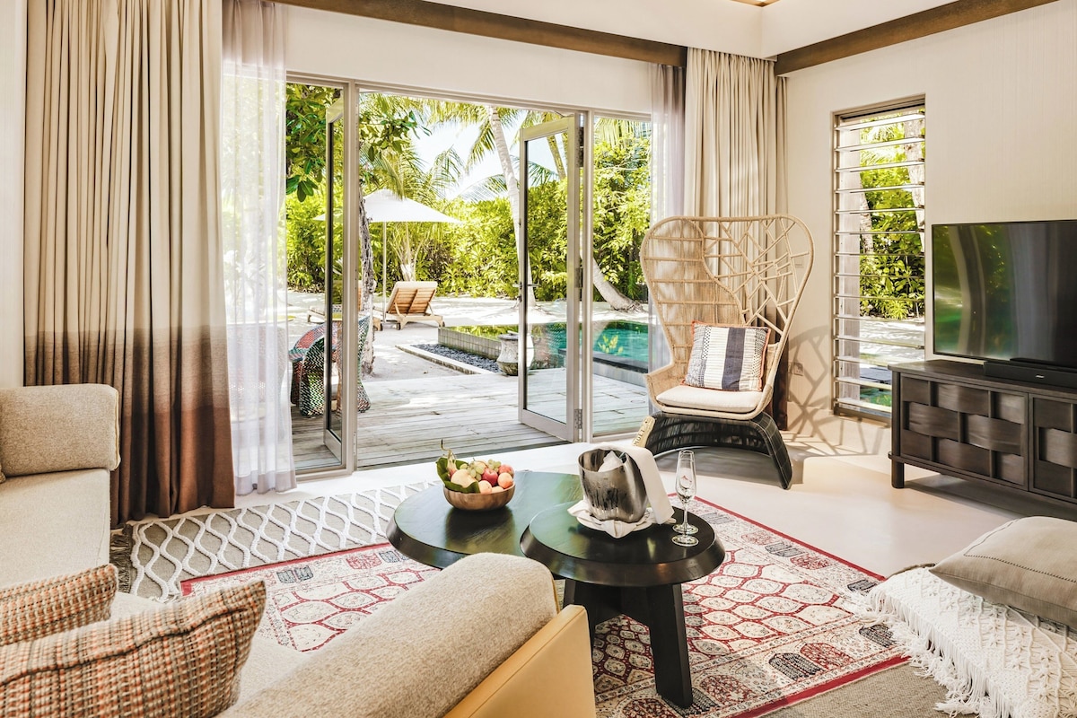 A spacious living room with a large TV, comfortable seating, a dining area, and a view of an outdoor pool area.