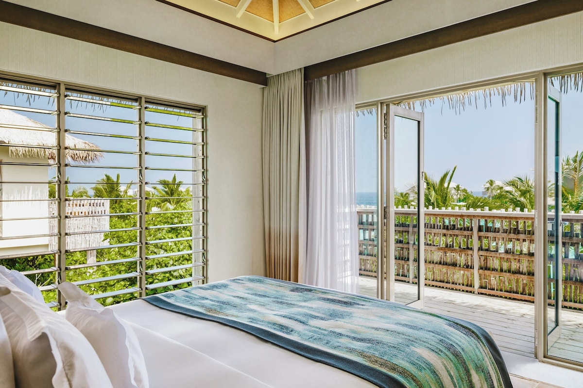 A hotel room with a bed, a view of the ocean, and a balcony with a railing.