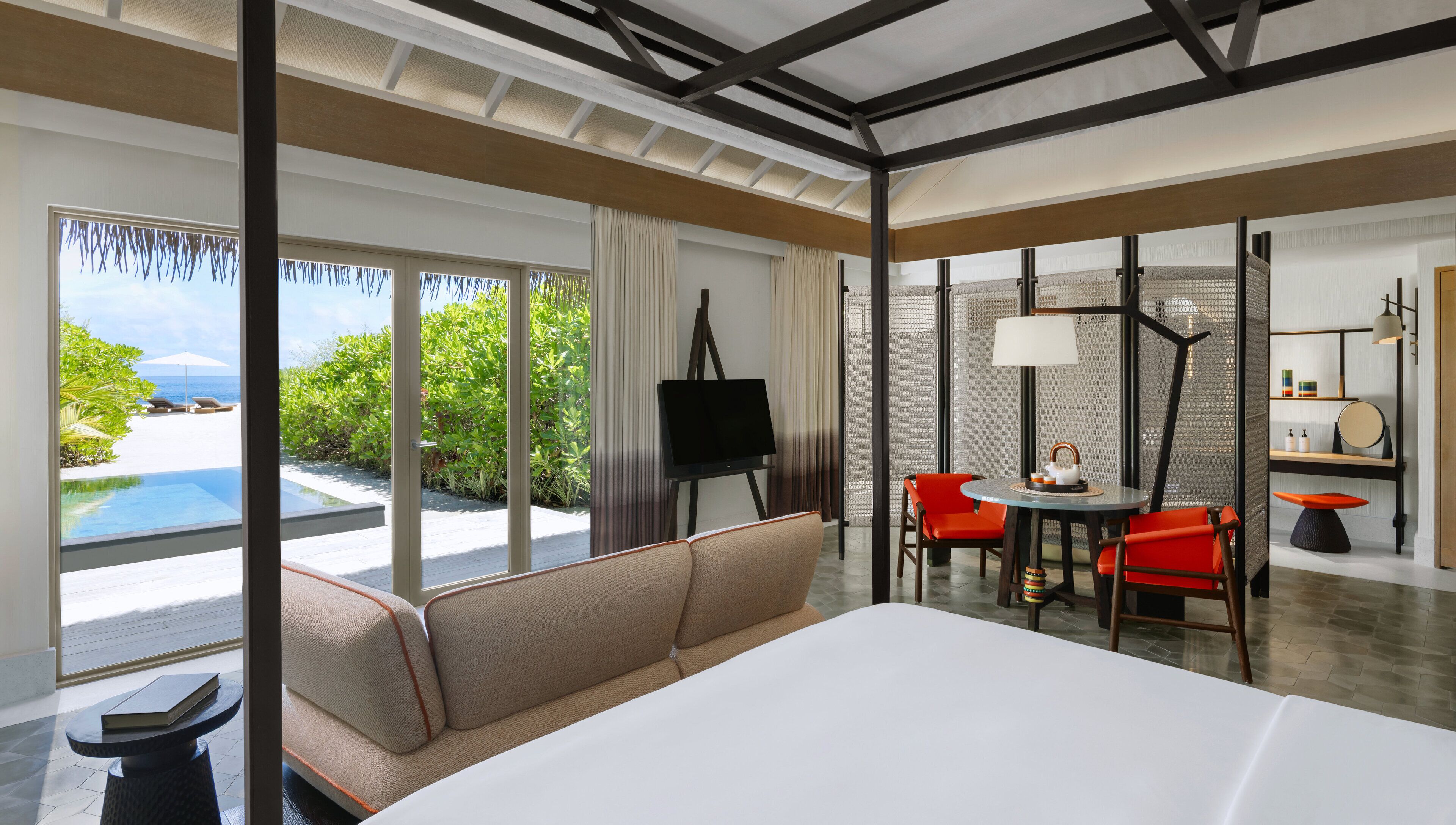 Une chambre d’hôtel moderne dotée d’un grand lit, d’un canapé, d’une table à manger avec des chaises, d’un tableau sur chevalet et offrant une vue sur l’océan.