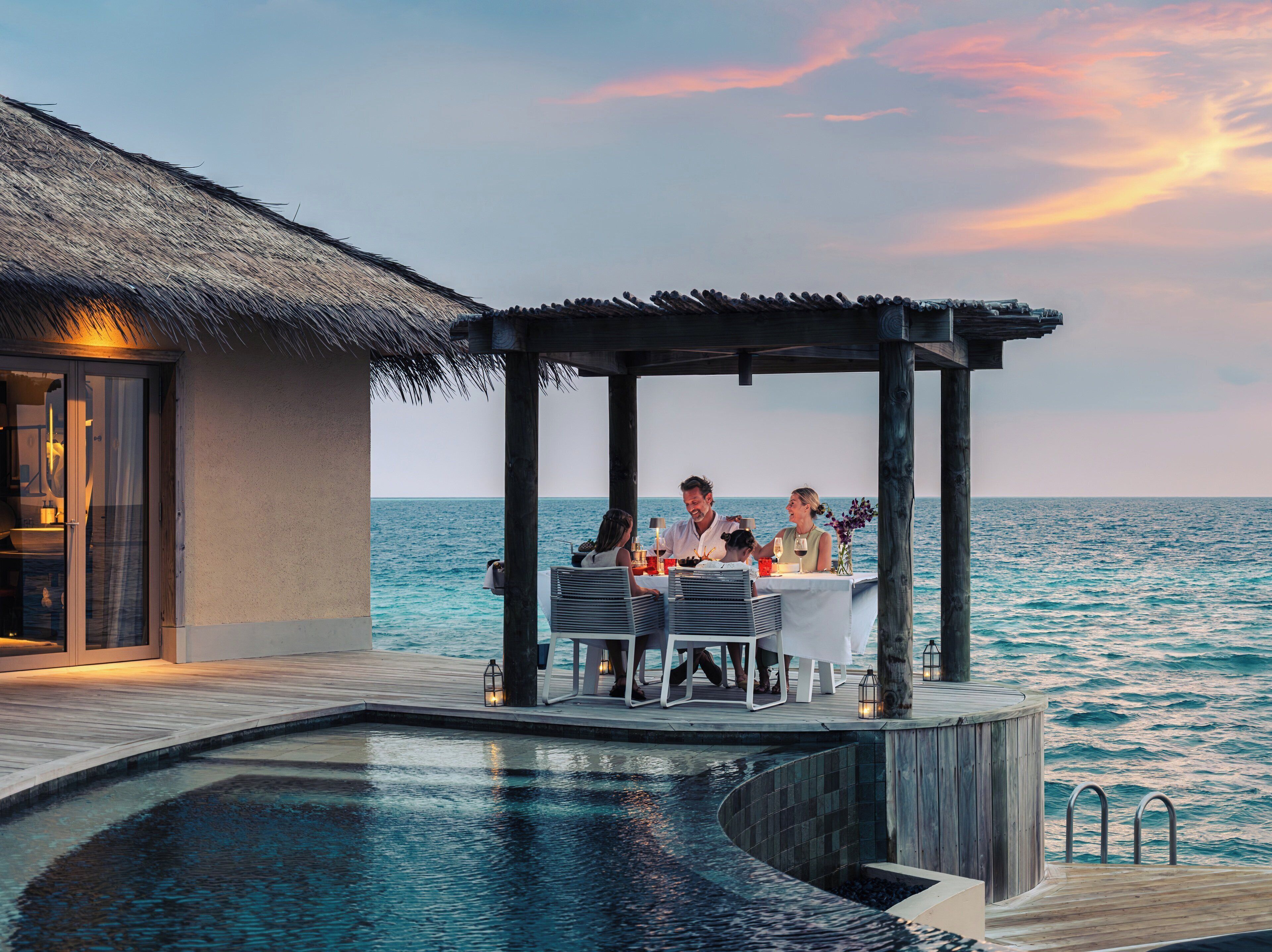 A couple dining at an outdoor table by a pool with a view of the ocean.