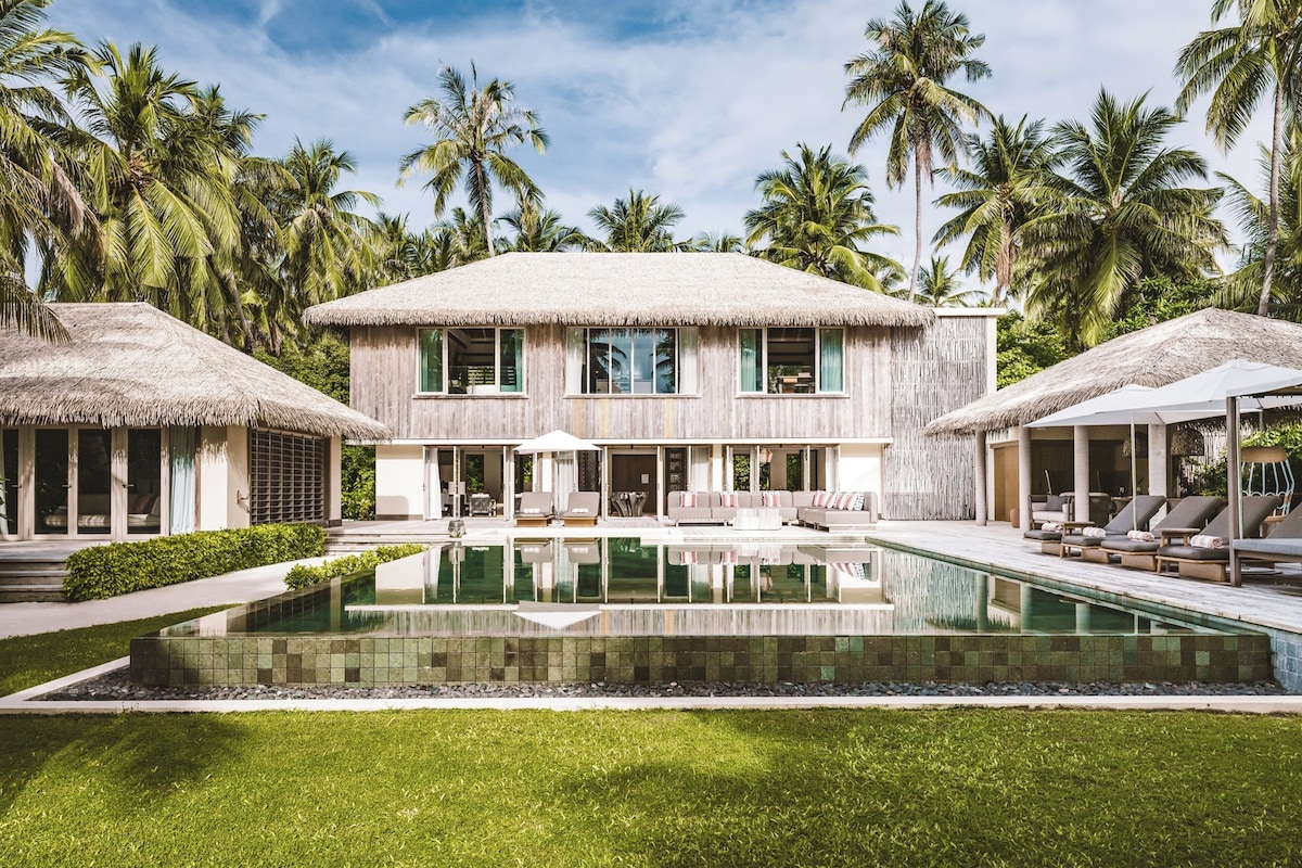 A resort with a pool, thatched-roof structures, and palm trees.