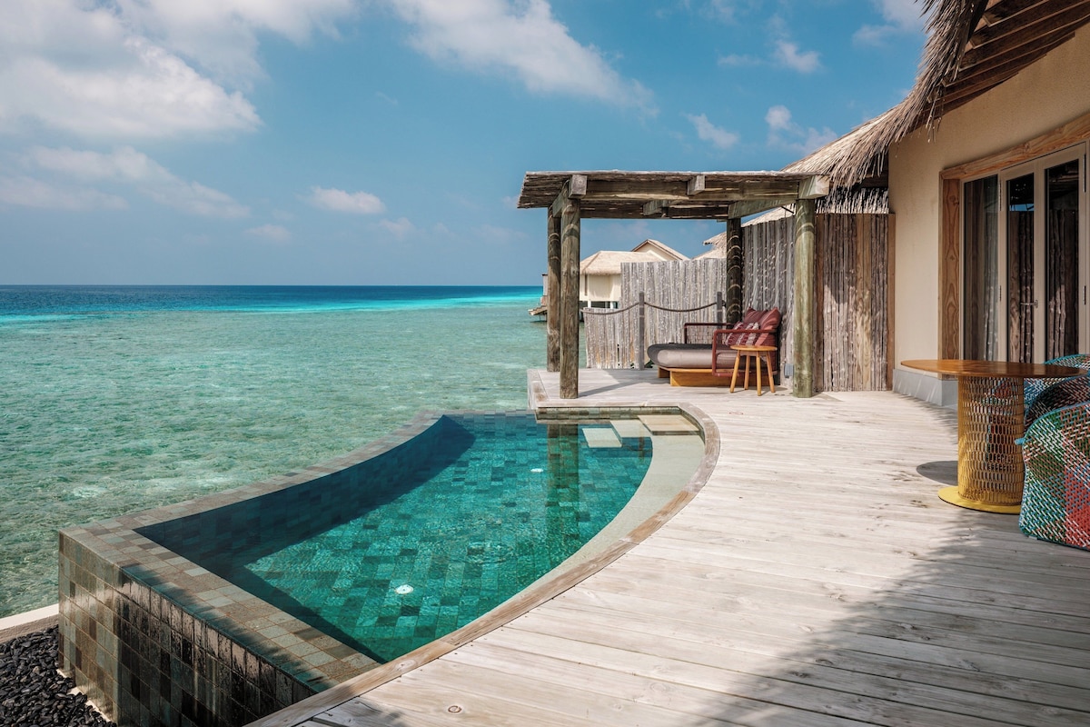 A wooden deck with a clear pool, a thatched-roof structure, and a view of the ocean.