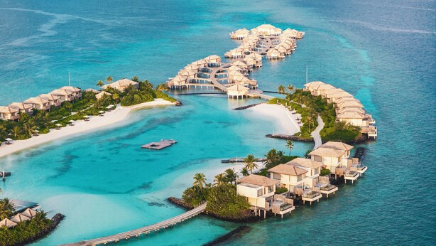 An aerial view of a resort with overwater bungalows connected by walkways, a sandy beach, and clear turquoise waters. - InterContinental Maldives Maamunagau Resort by IHG (Maamunagau Island)