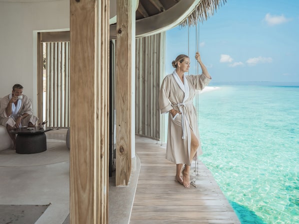 A wooden deck with a view of the ocean, a person in a robe, and another person in the background.