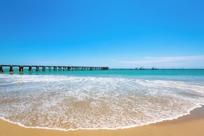 A beach with a wooden pier extending into the water, clear skies, and calm sea.