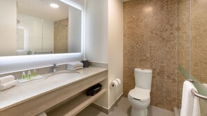 A modern bathroom with a large mirror, a sink with toiletries, a toilet, and patterned tiles. - Holiday Inn Piura by IHG (Piura)