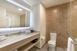 A modern bathroom with a large mirror, a sink with toiletries, a toilet, and patterned tiles.