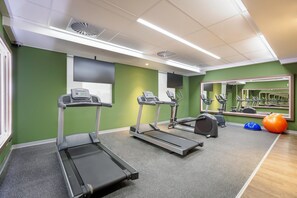 Une salle de sport équipée de tapis de course, de vélos d’exercice et d’un grand miroir.