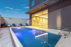 A swimming pool with a clear blue water surface, surrounded by lounge chairs and a glass wall leading to a well-lit interior space. - Holiday Inn Piura by IHG (Piura)