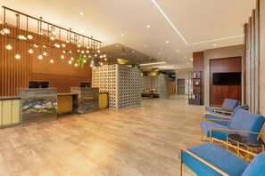 Eine Hotelhalle mit Empfangstresen, Sitzgelegenheiten und dekorativer Beleuchtung.
