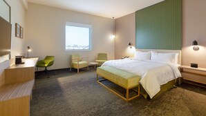 A hotel room with a bed, a desk, two chairs, a small table, and a window with a city view. - Holiday Inn Piura by IHG (Piura)