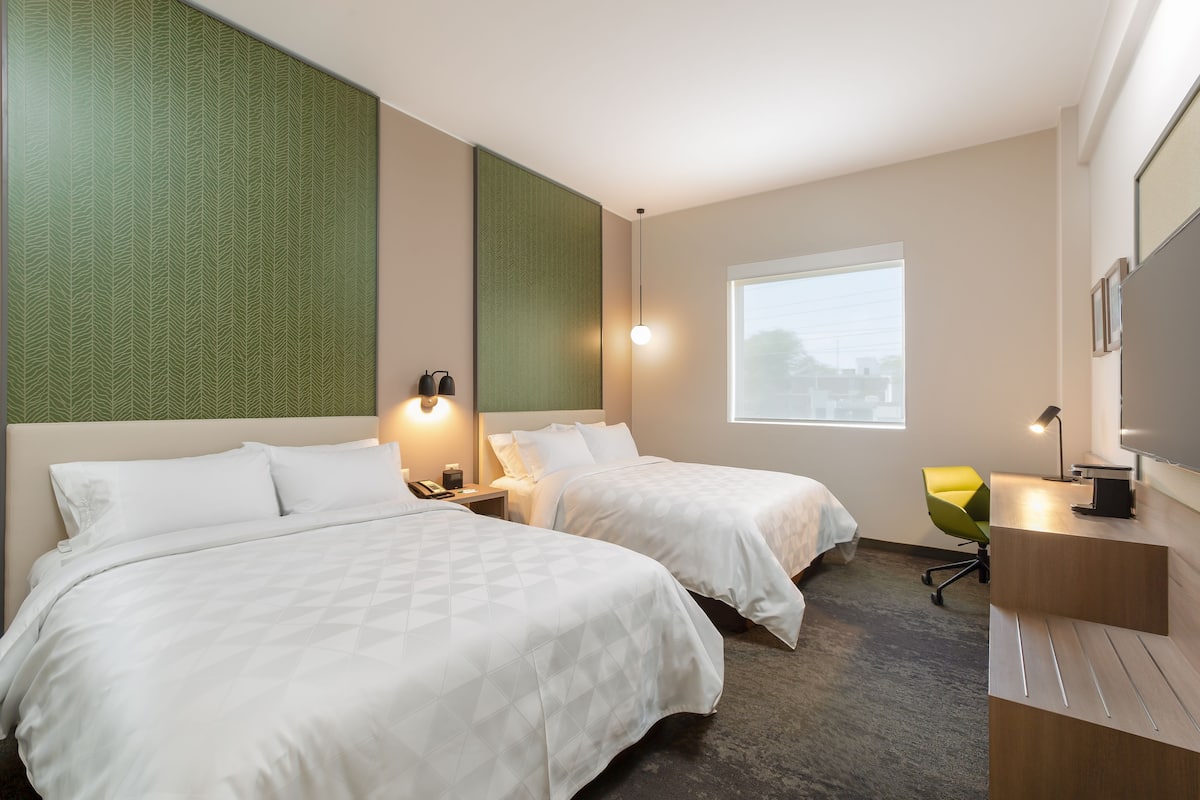 A hotel room with two beds, a desk, a chair, a TV, and a window.