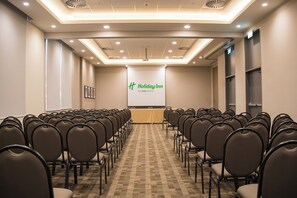 Ein Konferenzraum mit Reihen von Stühlen, die auf einen projizierten Bildschirm zeigen, der die Marke 'Holiday Inn' präsentiert.