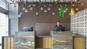 A reception desk with a marble top, a modern wooden wall with slats, and a geometric white partition. - Holiday Inn Piura by IHG (Piura)