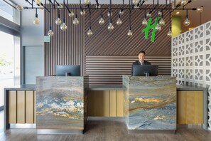 A reception desk with a marble top, a modern wooden wall with slats, and a geometric white partition. - Holiday Inn Piura by IHG (Piura)