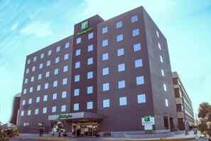 Un hôtel Holiday Inn à plusieurs étages, doté d’un design moderne, avec une entrée imposante et un ciel dégagé en arrière-plan.