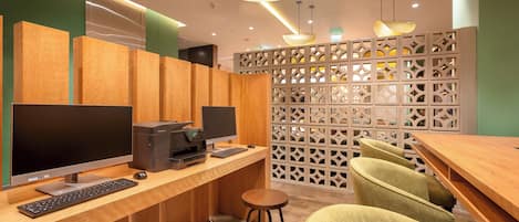 Een moderne werkruimte met houten bureaus, computers en een afgescheiden zithoek met groene stoelen.