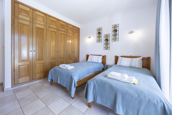 A hotel room with two beds, a large wooden wardrobe, and wall-mounted artwork.