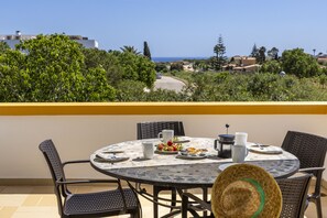 A round table with chairs, a hat, and a table setting with plates, cups, and a coffee pot on a balcony overlooking a coastal landscape. - Villa A Jardim Palmeiras Condominium by CoolHouses (Luz)
