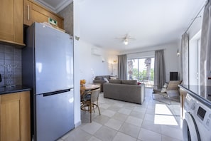 A modern kitchen with a built-in refrigerator, a dining area with a table and chairs, a sofa, and a balcony with a view.