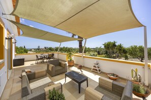 A sunlit outdoor patio with wicker furniture, a table, and potted plants.