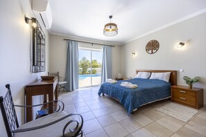 A bedroom with a bed, a desk, a chair, a nightstand, and a wall-mounted lamp.