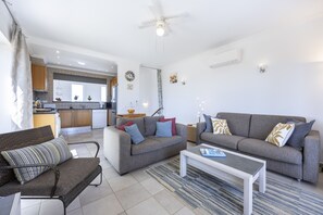 A modern living room with a grey sofa set, a coffee table, and a dining area with a kitchen in the background.