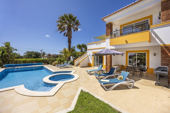 A pool area with a hot tub, lounge chairs, and a barbecue grill.
