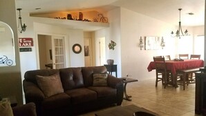 A living room with a brown sofa, a coffee table, and a dining area with a red tablecloth. - Clean 3 Bed/2 bath home w/ pool, BBQ & covered patio, locked RV & boat parking (Lake Havasu City)